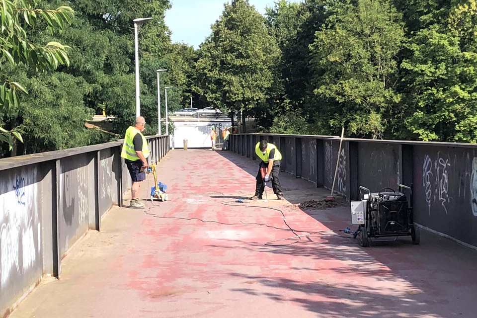 Op de fietsbrug over de Zuid-Willemsvaart worden de oude bovenlagen in asfalt handmatig verwijderd, een gigantisch werk. 