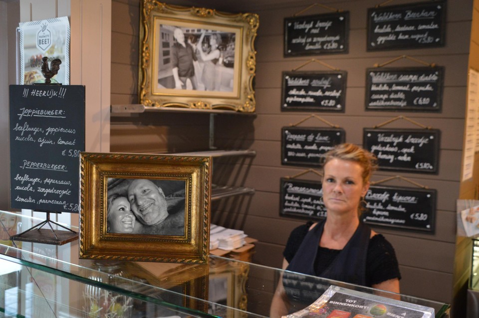 Sandy achter de toonbank, met vooraan een foto van haar en Ron in betere tijden.