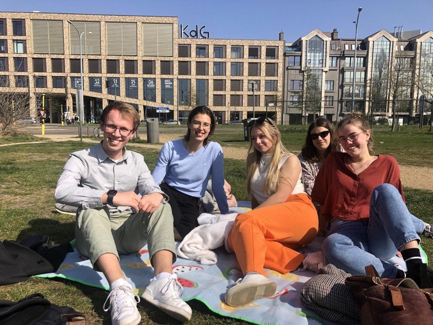 Chloé (blue sweater), Aline (orange pants) and Lise (red blouse) have lunch in the park near their campus. 