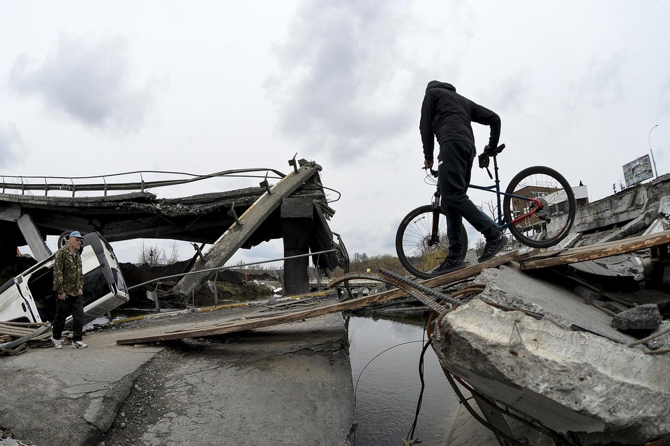 Een man probeert met een fiets een gebombardeerde brug over te steken in de Oekraïense stad Irpin, die inmiddels op Rusland is heroverd. 