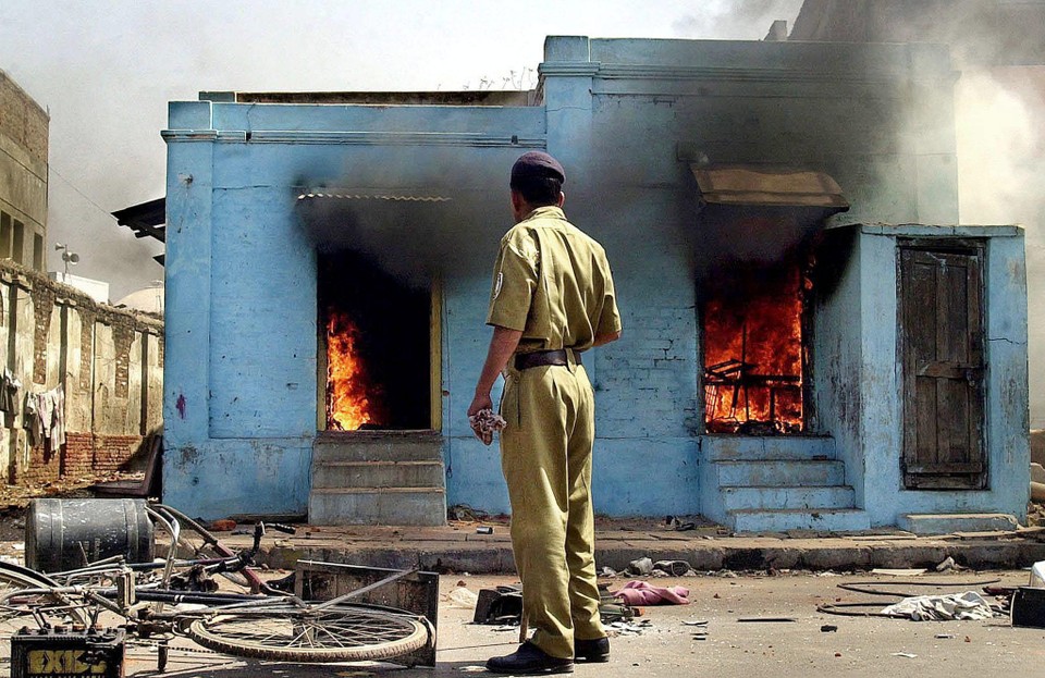 Een politieagent kijkt naar een winkel uitgebaat door moslims die in vlammen opgaat in Ahmedabad (Gujarat) in 2002