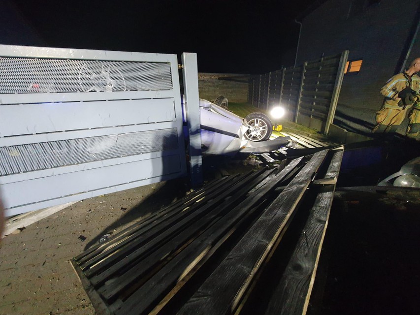 De auto ligt op zijn dak achter de poort. Twee houten panelen werden omvergereden.