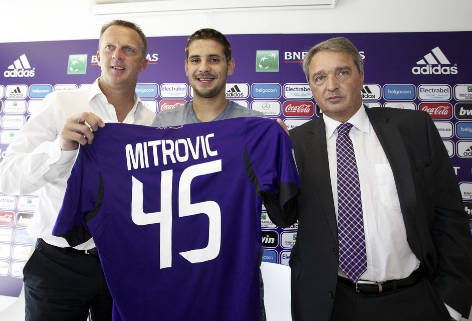 Mitrovic poseert met toenmalig Anderlecht-trainer John van den Brom en Herman Van Holsbeeck net na zijn handtekening bij Anderlecht eind augustus 2013. Zijn overgang naar Newcastle twee jaar later wordt onderzocht door het gerecht.  